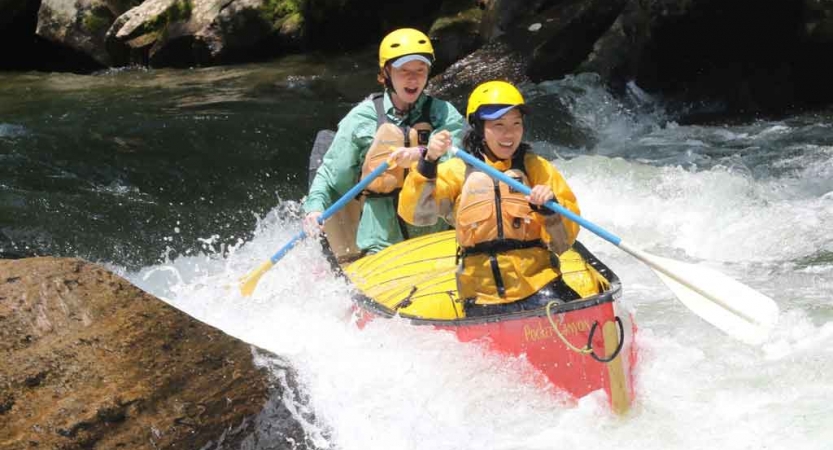 two people paddle a canoe through whitewater on an outward bound course in north carolina